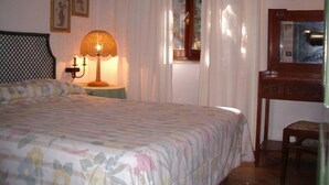A bedroom with a bed, a nightstand with a lamp, a dresser, and a window with curtains.