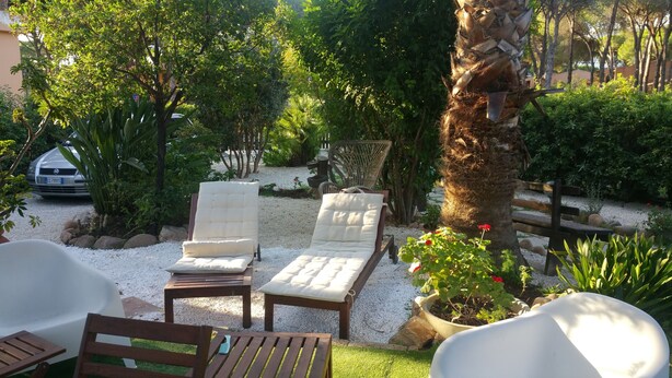 A garden with two cushioned lounge chairs, a wooden table, and a bench.