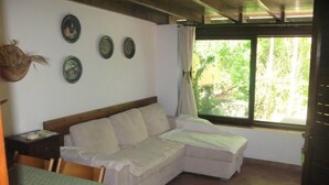 A room with a sofa bed, a small table with a book, and a window with a view of greenery.