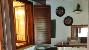 A rustic kitchen with wooden furniture, a tiled floor, and a window with wooden shutters.