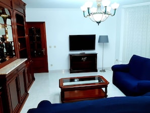 A living room with a TV, a sofa, a coffee table, and a chandelier.