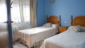 A room with two single beds, a wooden headboard, a nightstand, a window with sheer curtains, and a light switch on the wall. - Villa with panoramic views of the sea and the Rock of Ifach, with private pool. (Calpe)