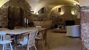 A rustic interior with stone walls, a stone bench, a table with chairs, and a television.