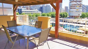 A balcony with a table and chairs, overlooking a pool and high-rise buildings. - Atico Ancla Penthouse (Benidorm)