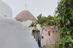 A traditional white building with a stone dome roof, a blue door, and a small garden area with plants and balloons.