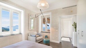 A modern bedroom with a large bed, a sofa, and a view of the sea. - Casa Mariavittoria - My Rental Homes (Massalubrense)