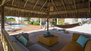 A covered outdoor seating area with a pool, a hammock, and a wooden deck.