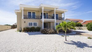 A two-story building with a balcony, a gravel driveway, and a palm tree.