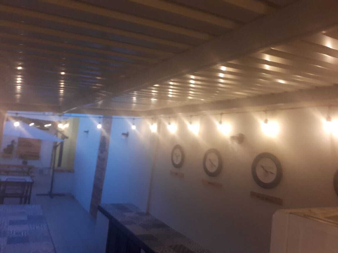 A dimly lit corridor with a ceiling that has a slatted design. There are wall-mounted clocks and string lights.