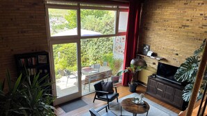 Un vaste salon doté d’une grande porte-fenêtre coulissante donnant sur un patio, d’une table basse en bois, d’un canapé et d’un téléviseur posé sur un meuble en bois.