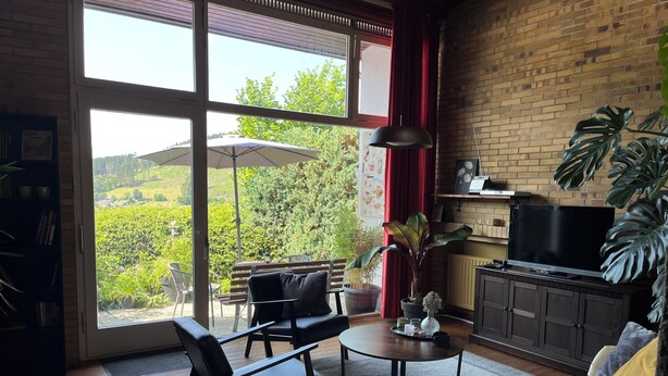 Un salon avec une grande fenêtre, un canapé, une table basse et un téléviseur.
