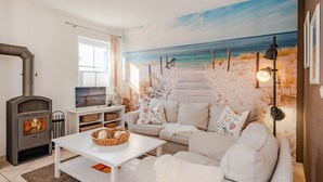 Un salon avec une fresque murale représentant une plage, une cheminée, un canapé et une table basse.