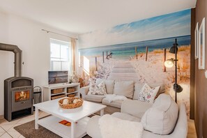 A living room with a beach mural, a fireplace, a sofa, and a coffee table. - Modern vacation home in Korswandt on the lake with large garden and fireplace (Korswandt)