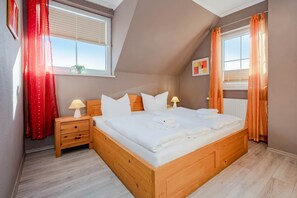 A bedroom with a wooden bed, two bedside tables, a window with blinds, and a radiator. - Modern vacation home in Korswandt on the lake with large garden and fireplace (Korswandt)