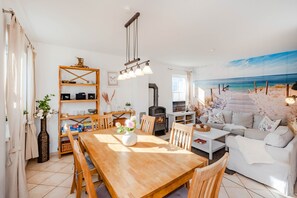 A cozy living room with a wooden dining table, a sofa, and a painting of a beach scene. - Modern vacation home in Korswandt on the lake with large garden and fireplace (Korswandt)