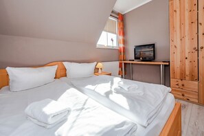 A neatly made bed with white linens and a folded towel, a bedside table with a lamp, and a television on a wooden stand. - Modern vacation home in Korswandt on the lake with large garden and fireplace (Korswandt)