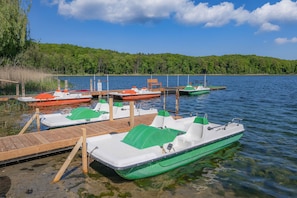 Un quai où sont amarrés plusieurs bateaux, une jetée en bois et une rive bordée d’arbres.
