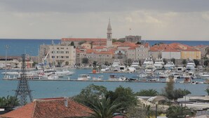 Un port de plaisance où sont amarrés de nombreux bateaux, une tour imposante et des bâtiments aux toits recouverts de tuiles rouges.