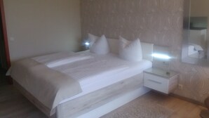 Ein modernes Schlafzimmer mit einem großen Bett, weißer Bettwäsche, einem Nachttisch mit Lampe und einem Wandpapier mit Muster.