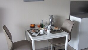 Ein Essbereich mit Tisch für zwei Personen, komplett mit Kaffeekanne, Tellern, Gläsern und einer Obstschale.