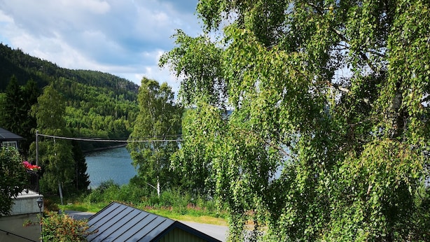A deck with wicker chairs overlooking a lake, surrounded by lush greenery and a small shed. - Idyllic vacation home right by the sea<br> (Docksta)