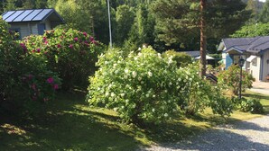 A residential area with a gravel driveway, a house with a blue roof, and a garden with white and pink flowers. - Idyllic vacation home right by the sea<br> (Docksta)