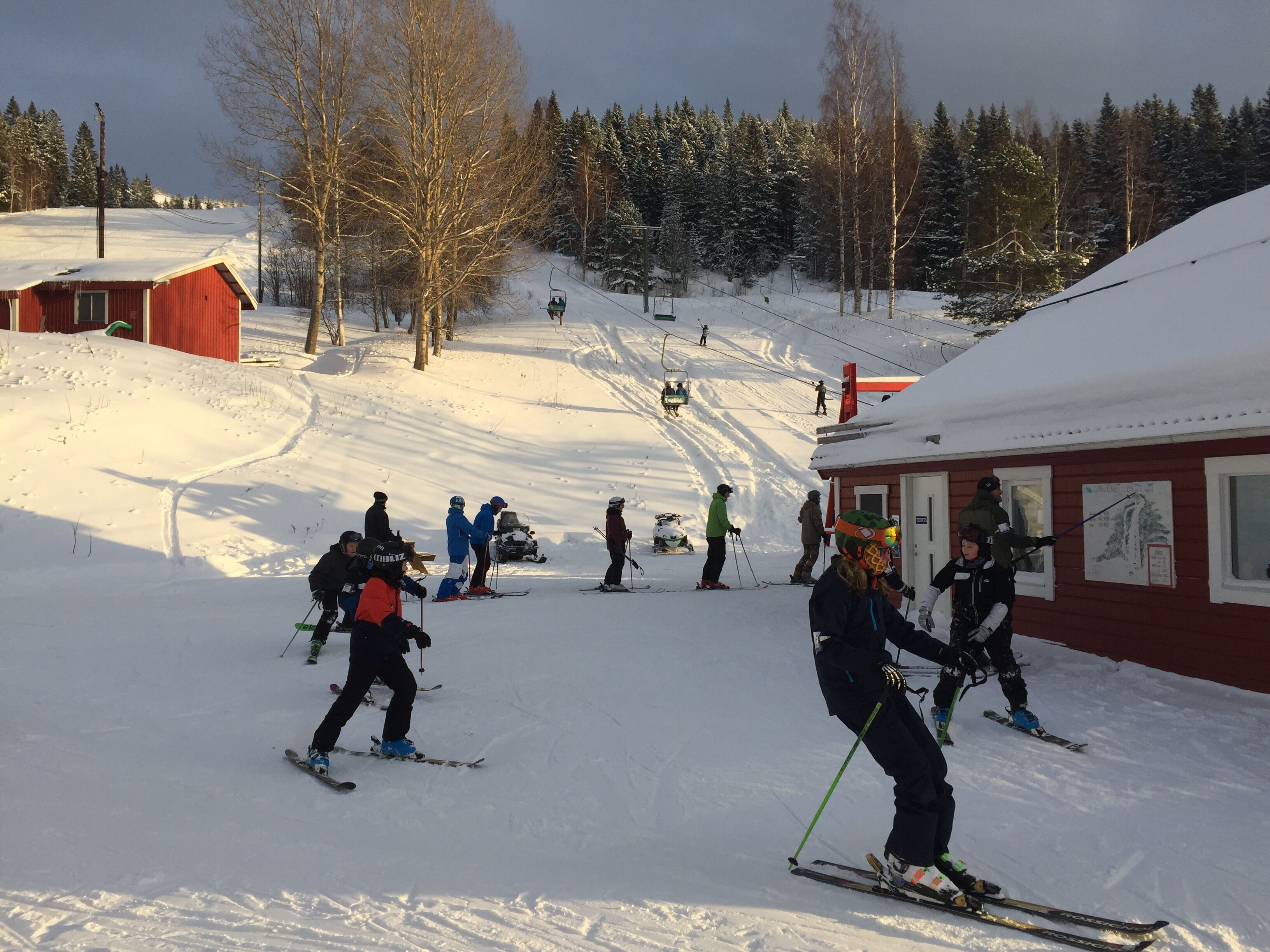A ski slope with skiers, a red building, and a ski lift in the background.