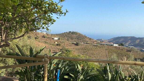 Una terrassa amb dos gandules blaus i blancs, una pèrgola de fusta i vista a un paisatge amb turons sota un cel serè.