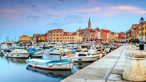 A marina with boats docked along a stone quay, surrounded by colorful buildings and a prominent tower in the background. - Apartment Lella near the sea and city center 500 meters (Rovinj)