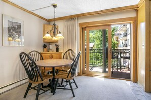 Un coin repas avec une table ronde et quatre chaises, un lustre, un buffet en bois et une porte-fenêtre coulissante donnant sur une terrasse extérieure.