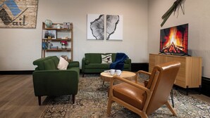 Un salon chaleureux avec un canapé vert, un fauteuil en cuir, une petite table ronde avec des tasses, une bibliothèque et deux tableaux abstraits.