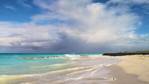 Una playa con agua turquesa cristalina, una orilla arenosa y un promontorio rocoso a lo lejos.