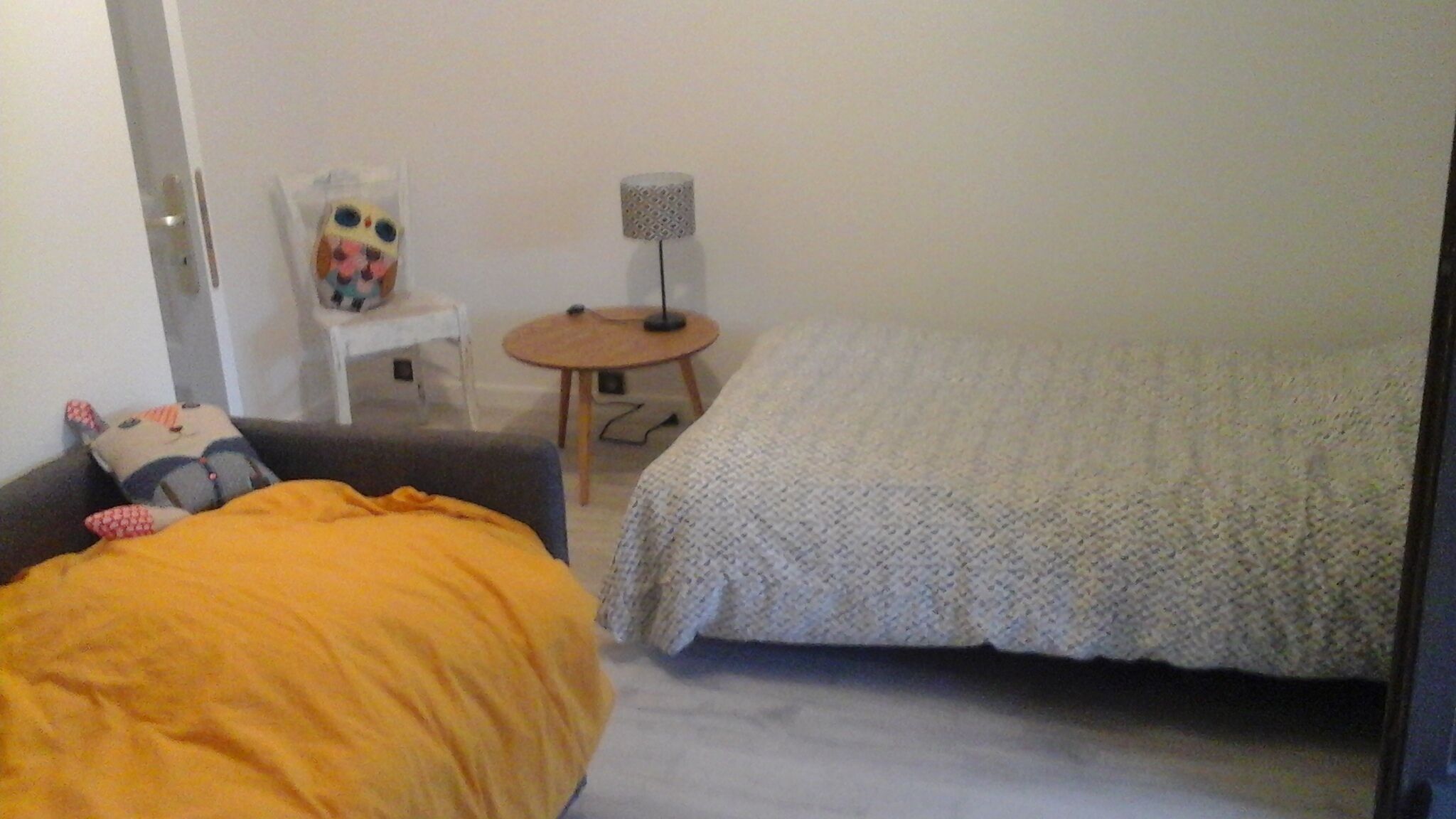 A room with two beds, a small table, a lamp, and a chair.