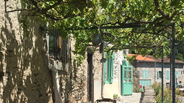Un espace de restauration en plein air, délimité par des murs en pierre, avec une table dressée pour deux personnes, une chaise et un coussin bleu posé sur le sol.