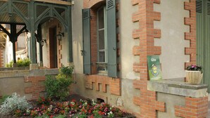 A building with brick walls, green shutters, and a flower bed with various flowers.