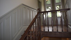 A wooden staircase with white wainscoting and a view of a room with a door and windows.