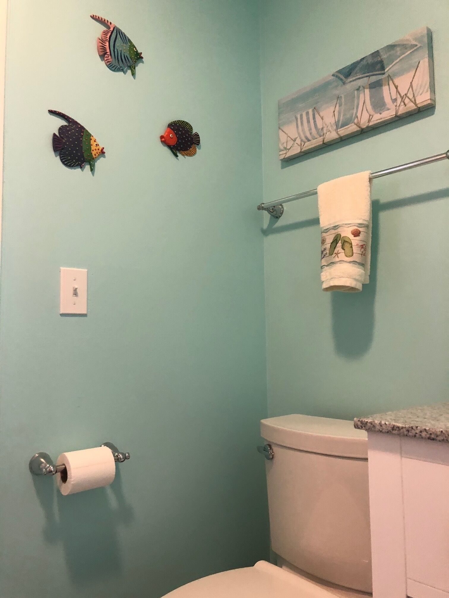 A bathroom with a toilet, a towel rack with a towel, and three decorative fish on the wall.