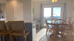 Un coin repas avec des chaises en bois et une table, une kitchenette avec une porte blanche, et un balcon avec vue.