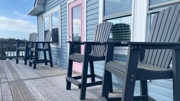 Une terrasse en bois avec des chaises Adirondack et un bâtiment doté d’une porte rose.