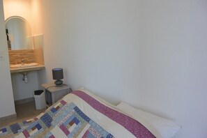 A bedroom with a bed, a bedside table with a lamp, a small trash bin, and a mirror above a sink. - FIUMICELLI - 3* - SEA VIEW - WI-FI (SOLENZARA)