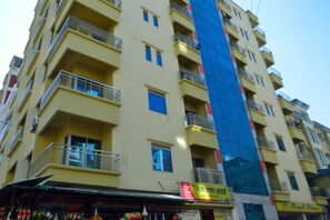 Un immeuble à plusieurs étages, doté de balcons et d’une façade en verre bleu, avec des vitrines au niveau du rez-de-chaussée.