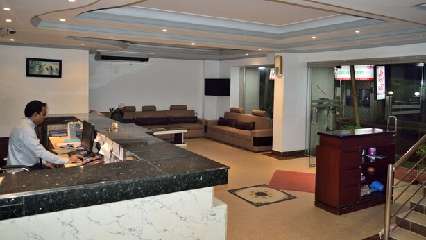 Ein Hotel-Rezeptionsbereich mit einer Marmor-Theke, Sofas, einem Fernseher und einer Treppe.
