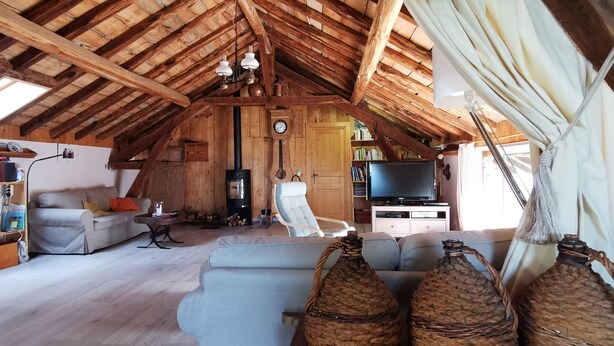 A cozy attic room with a wooden ceiling, a sofa, a television, and wicker baskets.