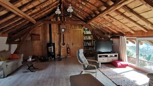 A cozy attic room with a wooden ceiling, a fireplace, a television, and a bookshelf.