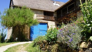 A rustic stone house with a blue door, a balcony, and a stone wall garden.