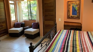 Una habitación con una cama, dos sofás, un ventanal con cortinas, una puerta y un cuadro enmarcado en la pared.