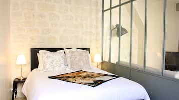 Una cama bien hecha con un cojín decorativo y un cuadro enmarcado, una lámpara de noche y una pared de piedra.
