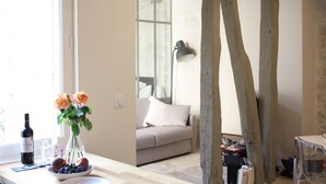 Une pièce avec un plafond orné de poutres en bois, une fenêtre offrant une belle vue, un canapé et une table sur laquelle sont posés un vase de fleurs et un saladier de fruits.