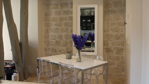 Un espace repas avec un mur en pierre, une table blanche et des chaises transparentes.