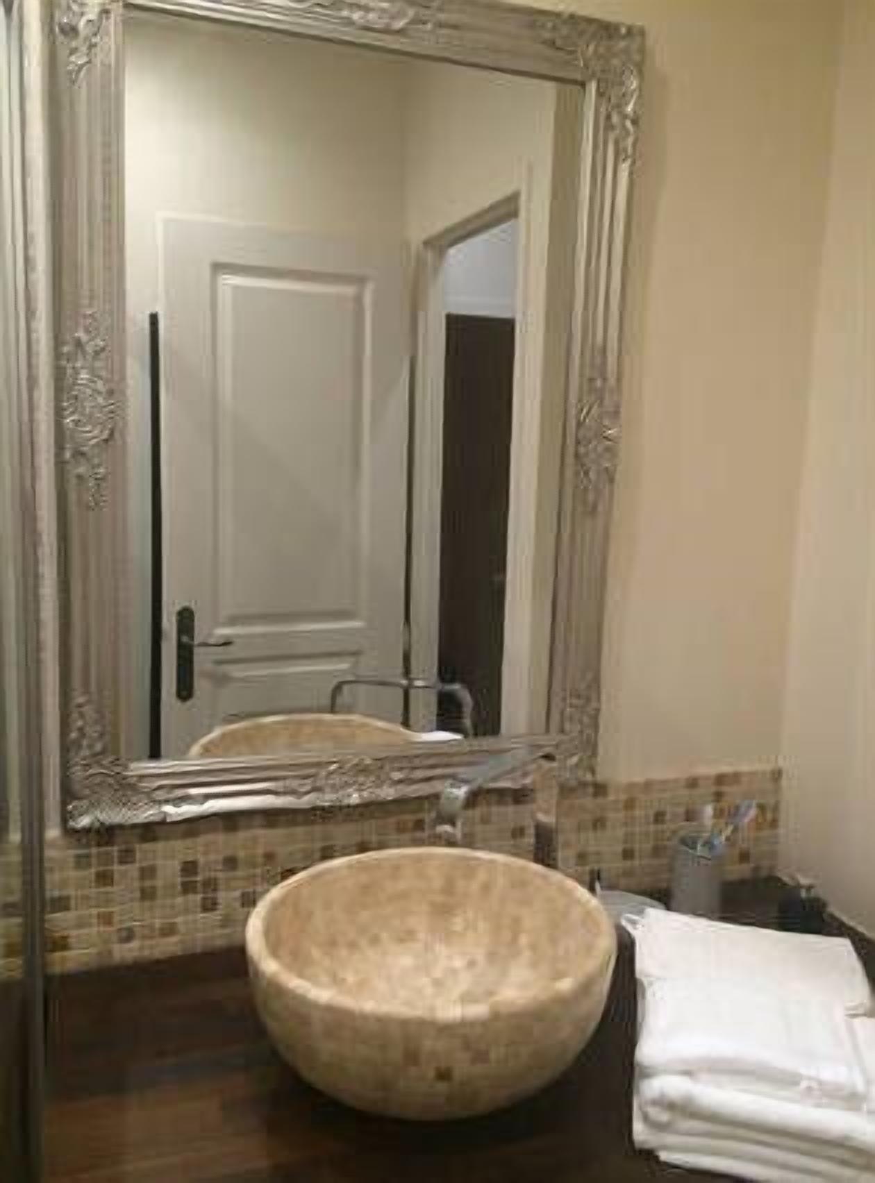 A bathroom with a large mirror, a round basin, and a tiled backsplash.